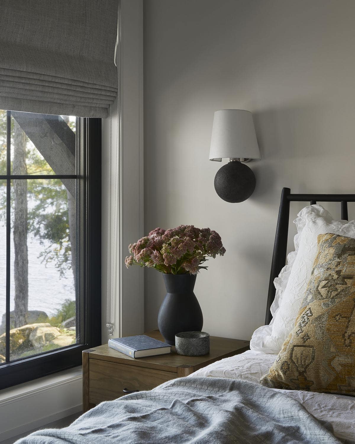 Bedroom nightstand with black vase, flowers, and lake view through window