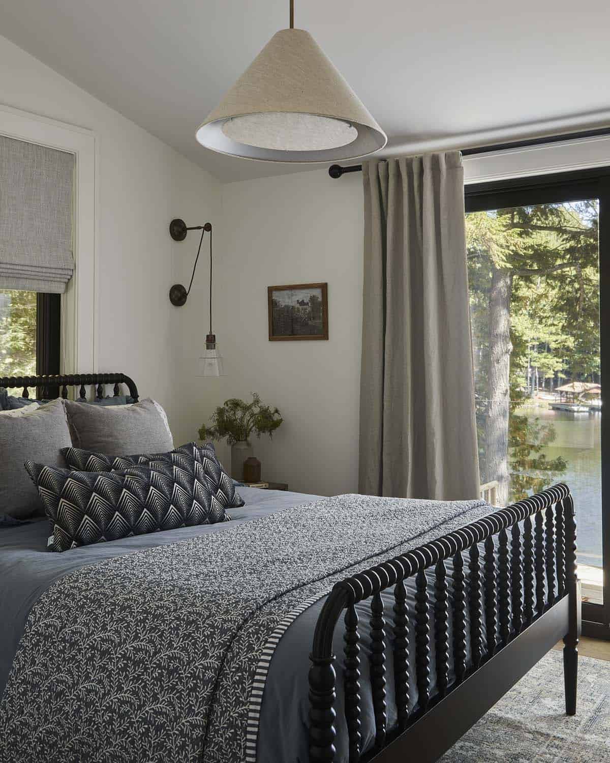 Bedroom with black spindle bed, layered patterned bedding, and lake view through glass doors