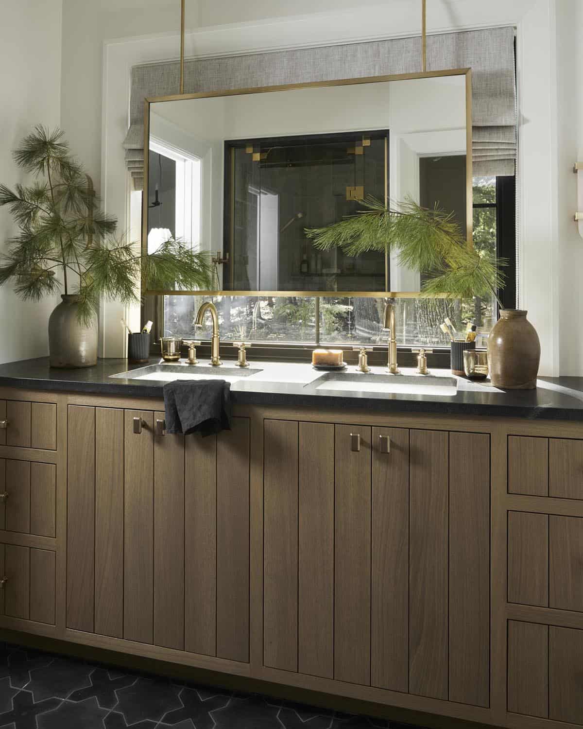 Bathroom double vanity with brass mirror, wood cabinetry, and black countertop