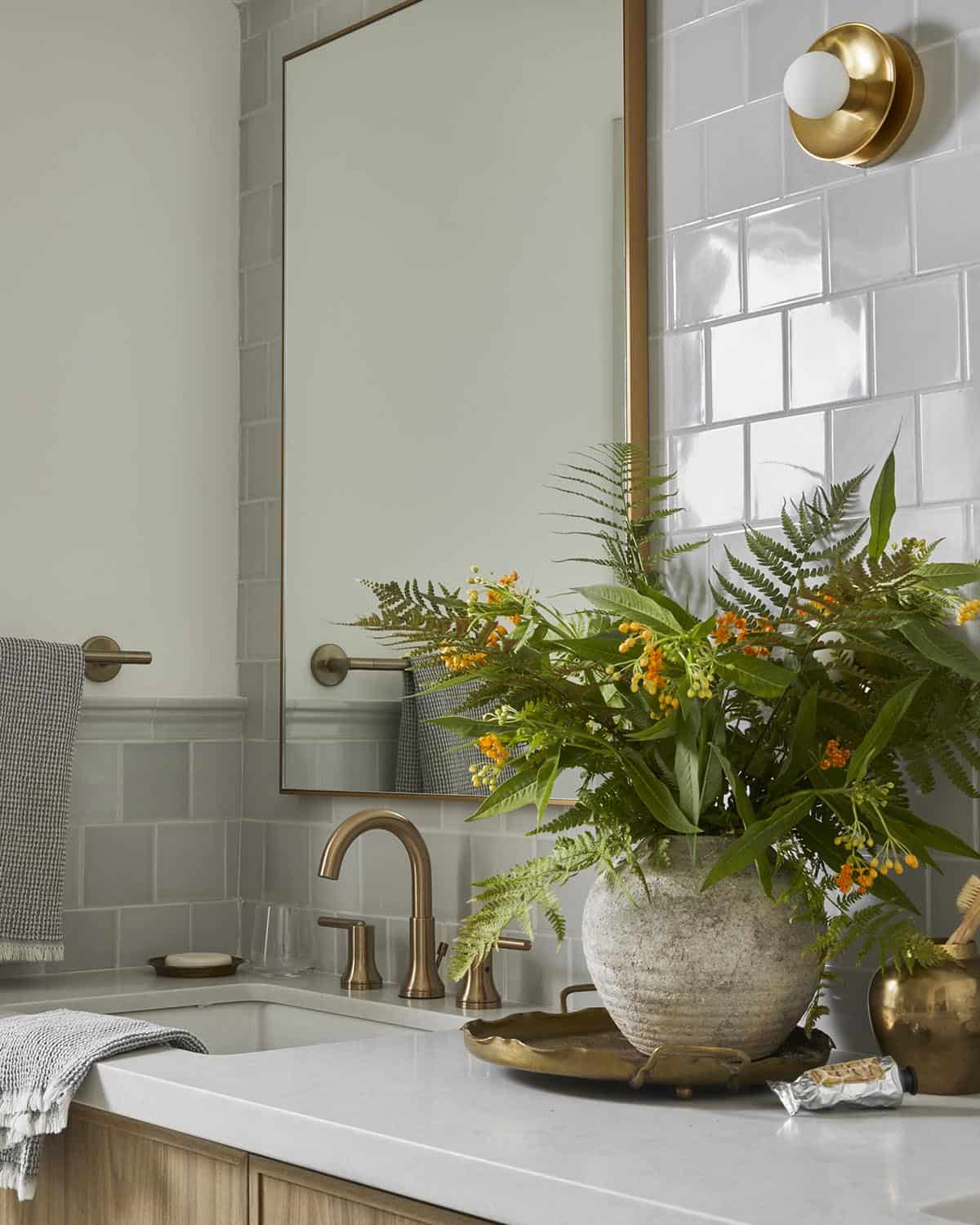 Bathroom vanity detail with brass faucet, subway tile, and fern arrangement