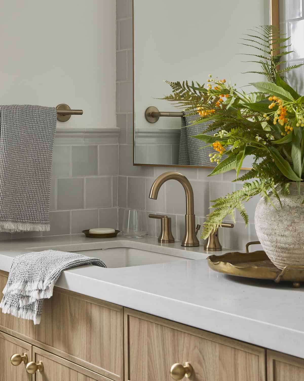 Bathroom vanity close-up with brass faucet, towel, and ceramic vase of ferns