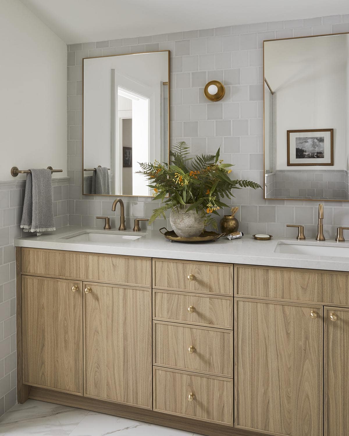 Double vanity bathroom with brass-framed mirrors, gray subway tile, and wood cabinets