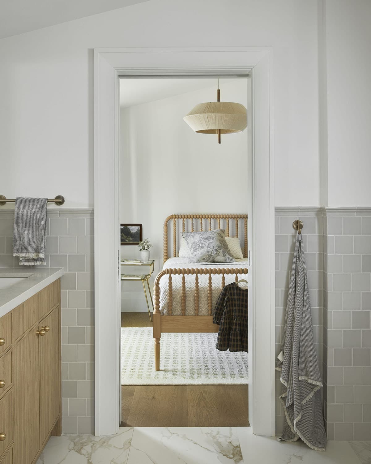 Doorway view from bathroom into bedroom with spindle bed and woven pendant light