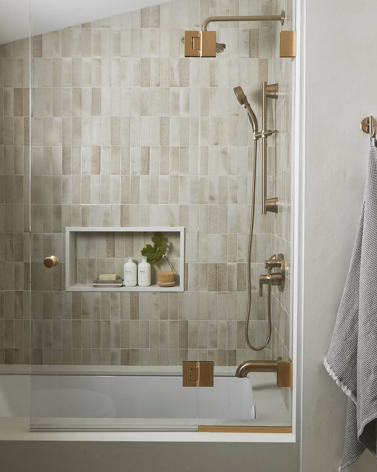 Shower with vertical zellige tile, brass fixtures, and built-in niche