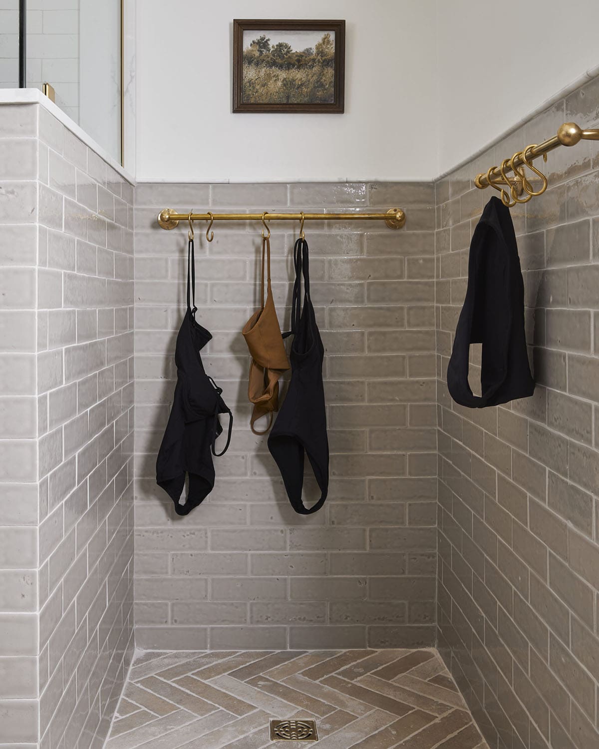 Bathroom nook with brass hooks holding swimsuits against tiled wall