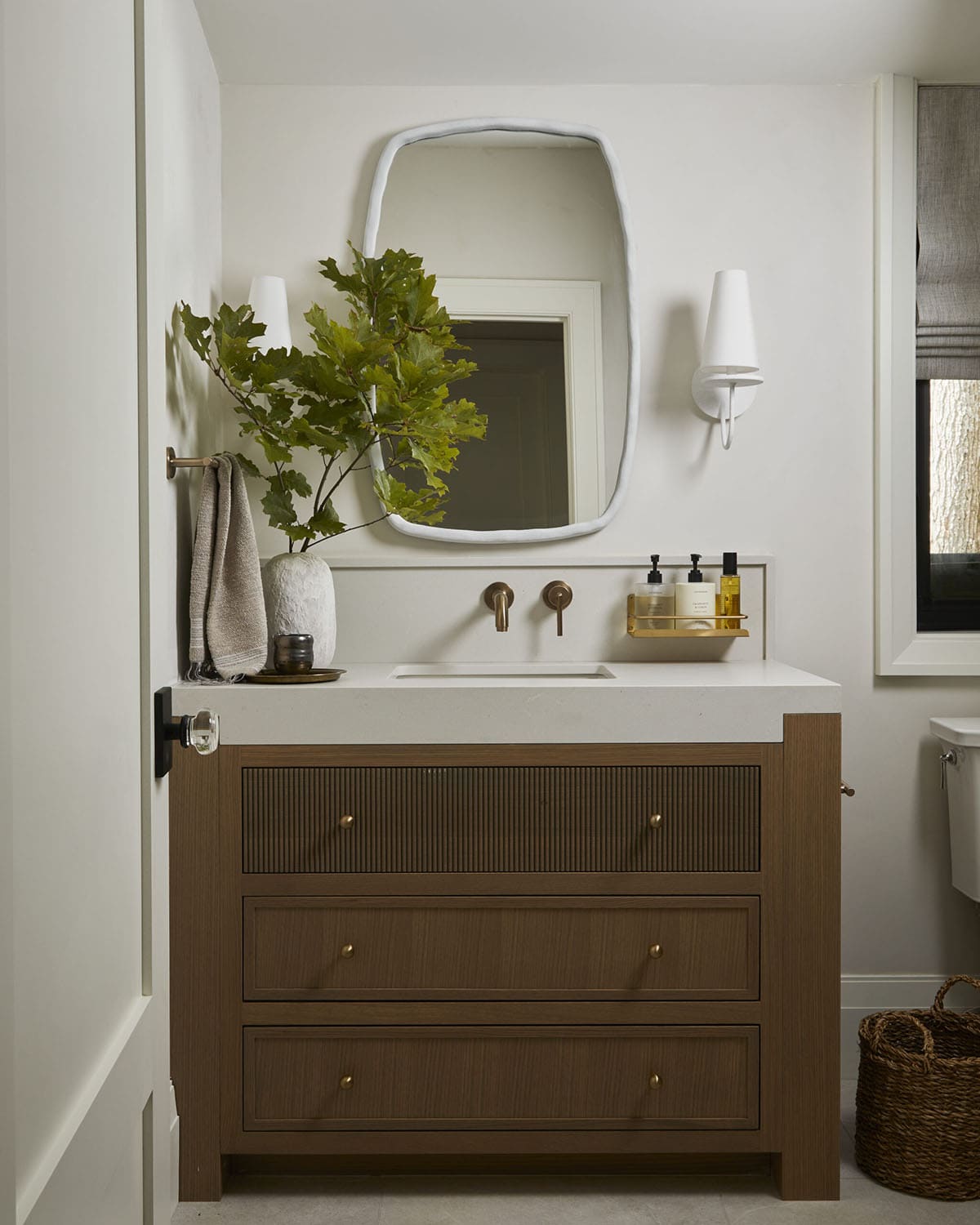 Powder room vanity with organic-shaped mirror, wood cabinet, and wall sconces