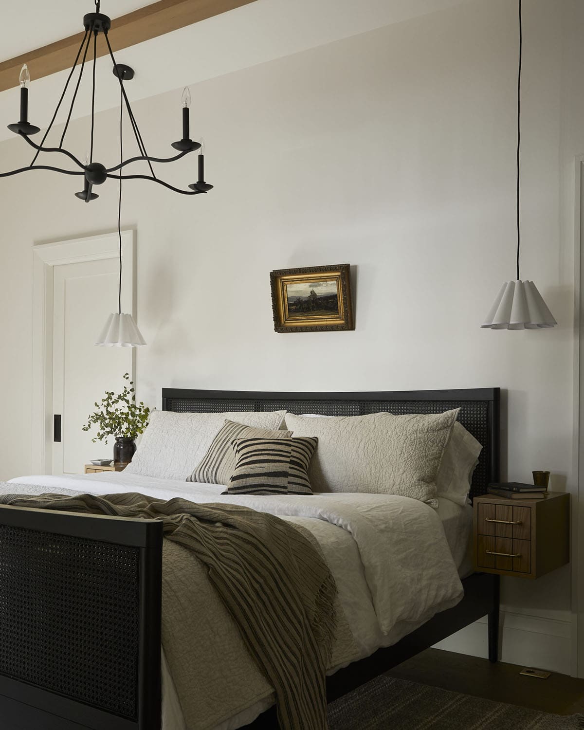 Bedroom with black candle chandelier, cane headboard, and floating wood nightstand