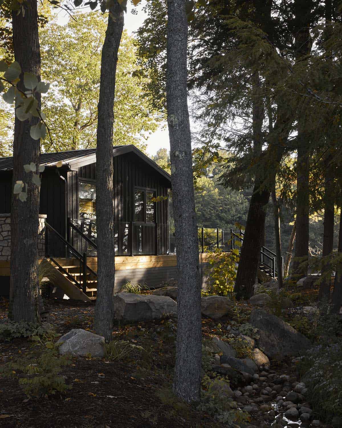Black cottage exterior among trees with wooden stairway and boulder landscaping