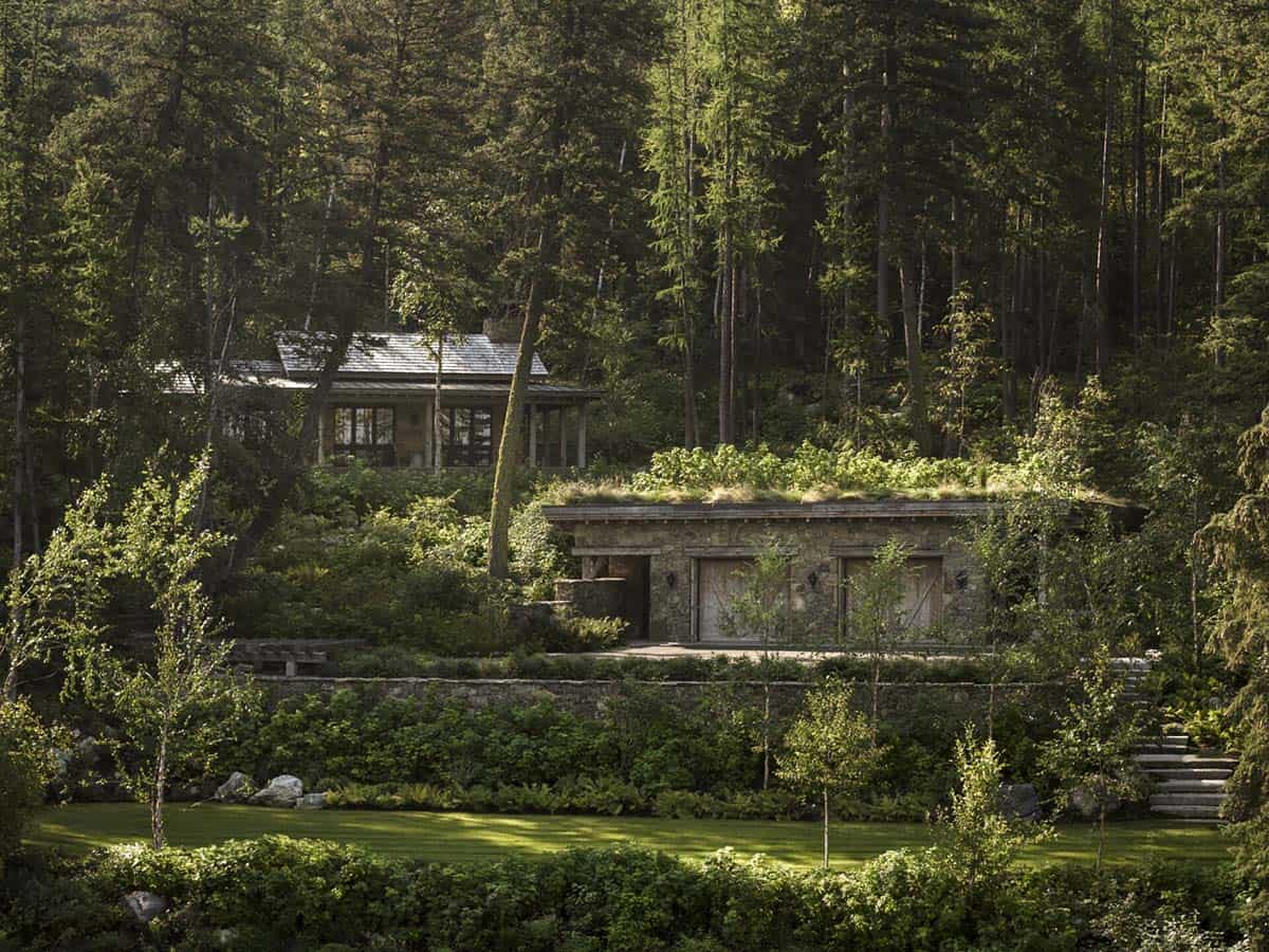Stone guest cabin and garage nestled in forested hillside above Whitefish Lake