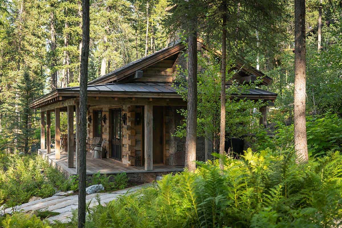 Log cabin with covered porch surrounded by ferns and pine trees