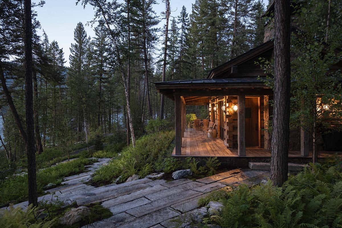 Covered porch of log cabin lit at dusk near lake