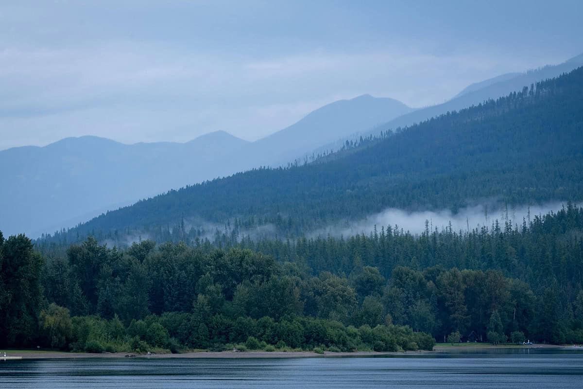 Misty mountain ridgeline above forested shoreline of Whitefish Lake