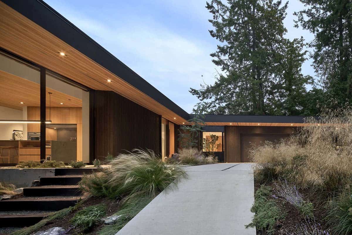 Dusk view of Layer House entrance with wood-clad carport and concrete steps leading up the slope