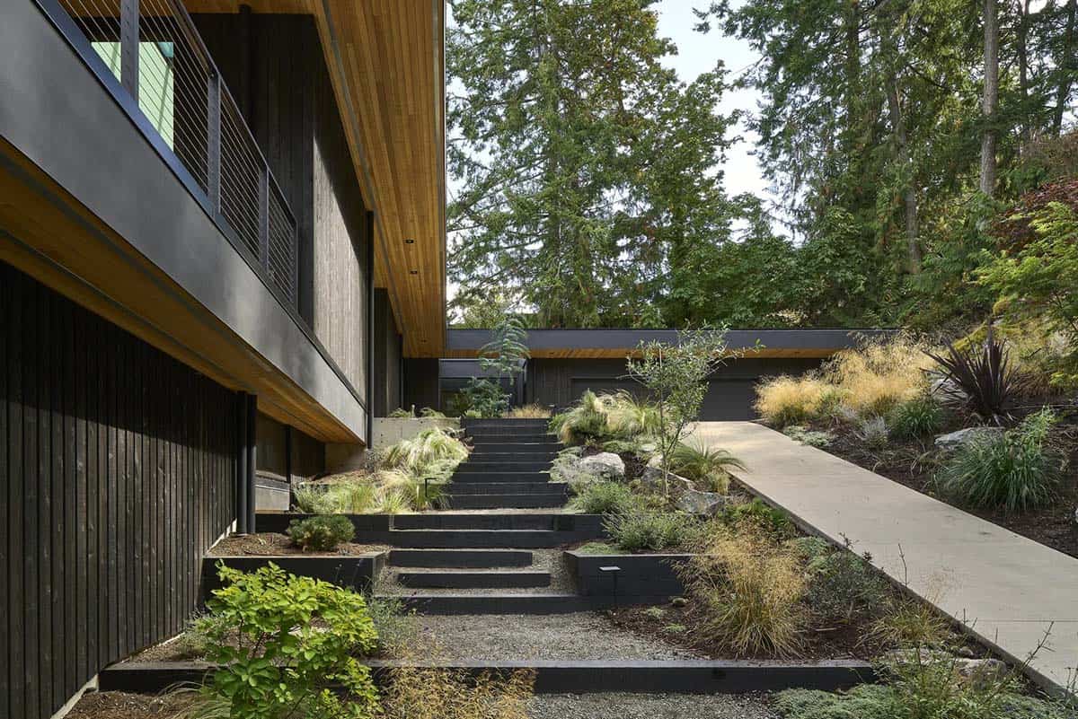 Black timber stair and steel-edged steps climbing the hillside beside Layer House
