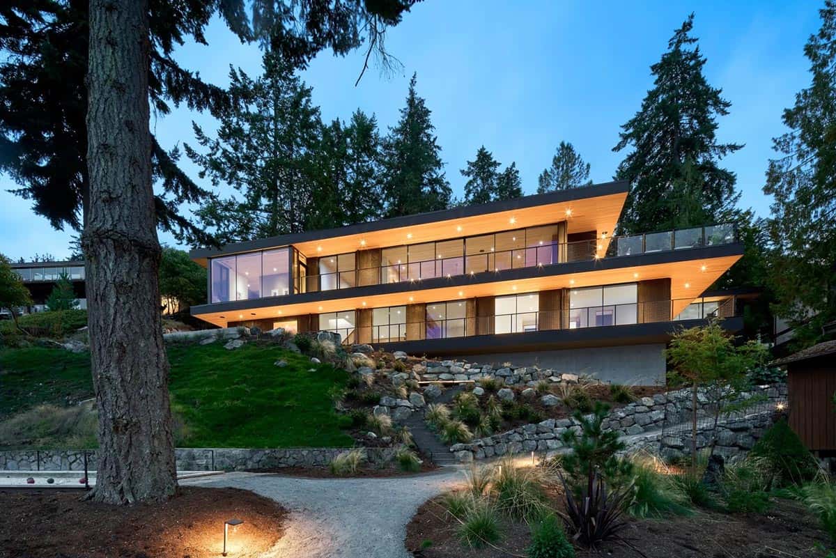 Layer House illuminated at dusk, stacked levels cantilevering above a stone-terraced slope