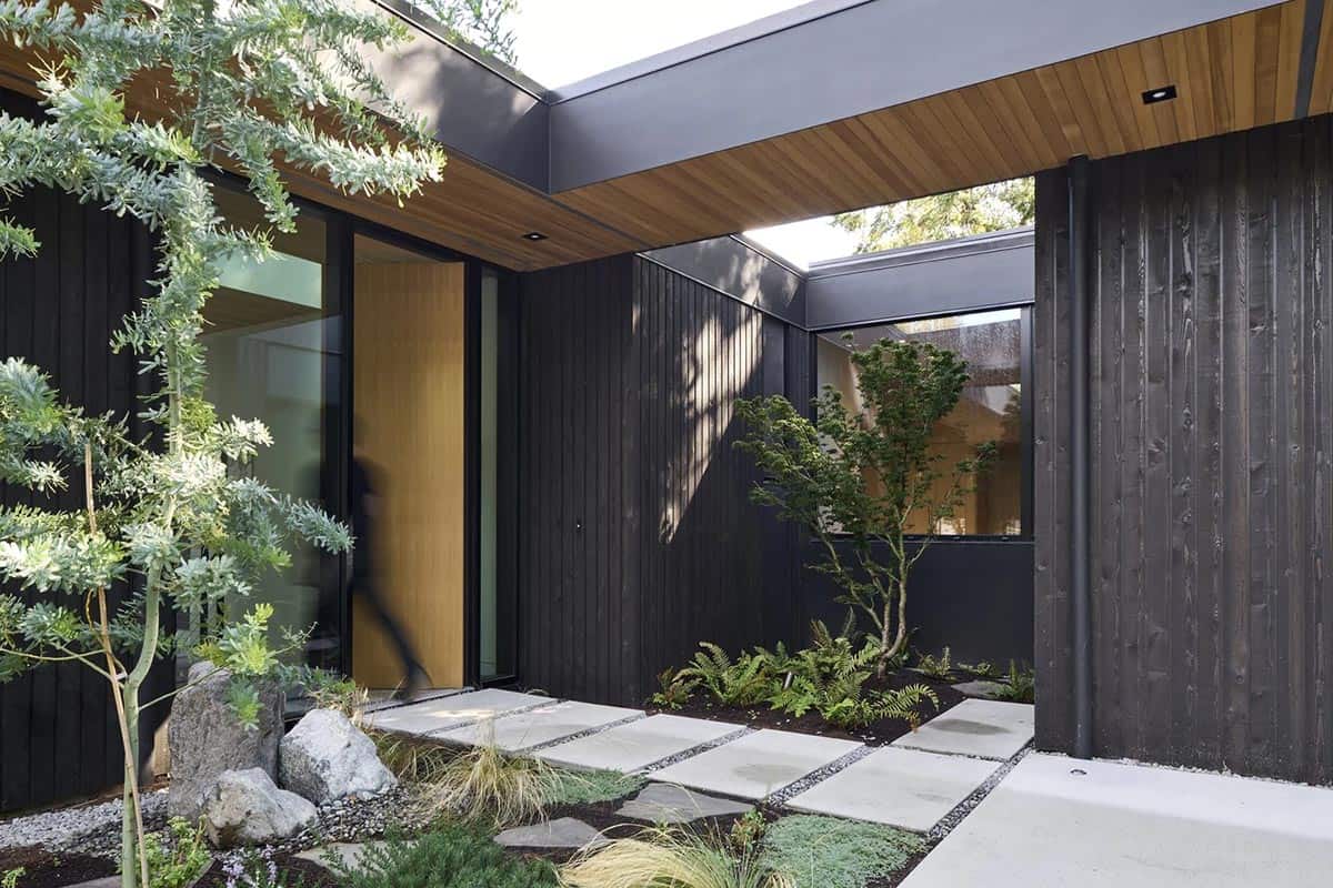 Entry courtyard of Layer House with charred wood siding and Japanese-inspired stone pathway