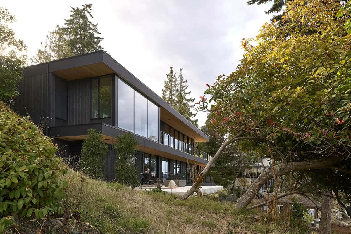 Layer House's dark timber facade rising above the forested, sloping waterfront site