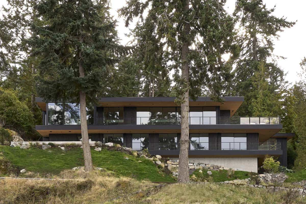 Layer House viewed through trees, its layered black volumes set into the slope