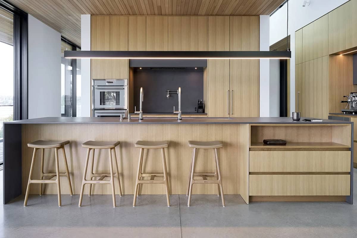 Wood-paneled kitchen island in Layer House with oak stools and matte black backsplash