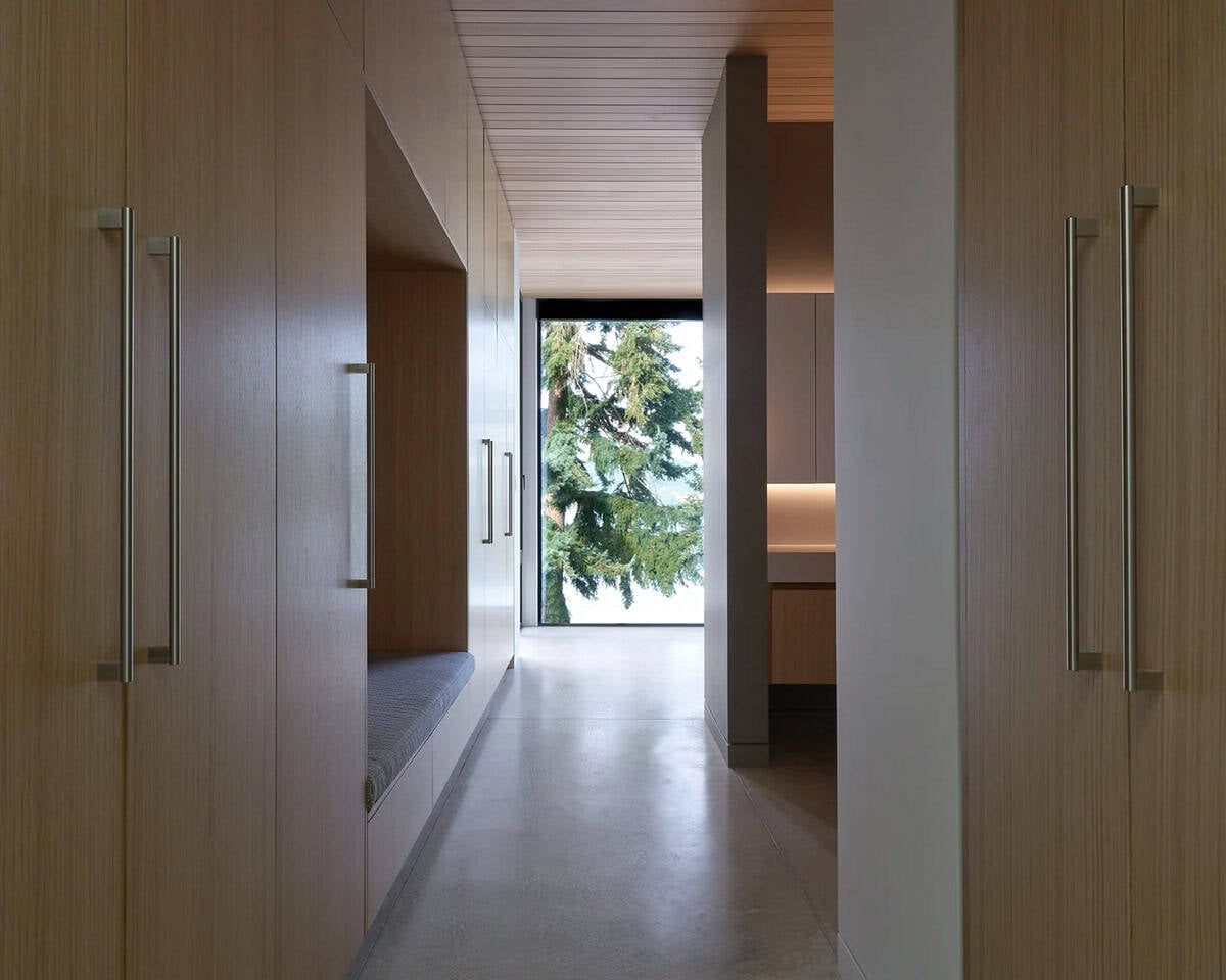 Wood-paneled hallway in Layer House with built-in bench and view of trees beyond