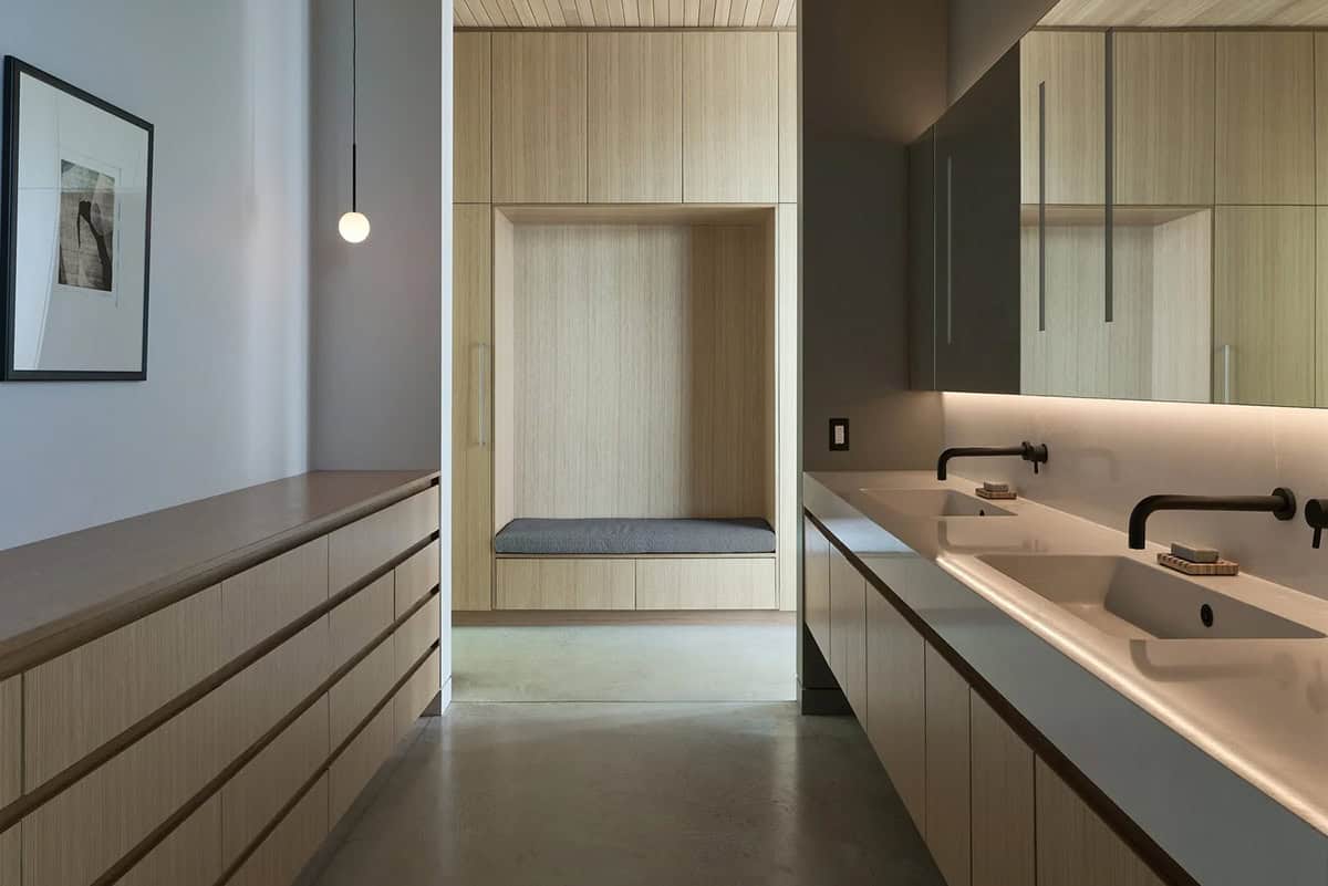 Walk-in closet with built-in seating nook opening onto a double-sink bathroom vanity