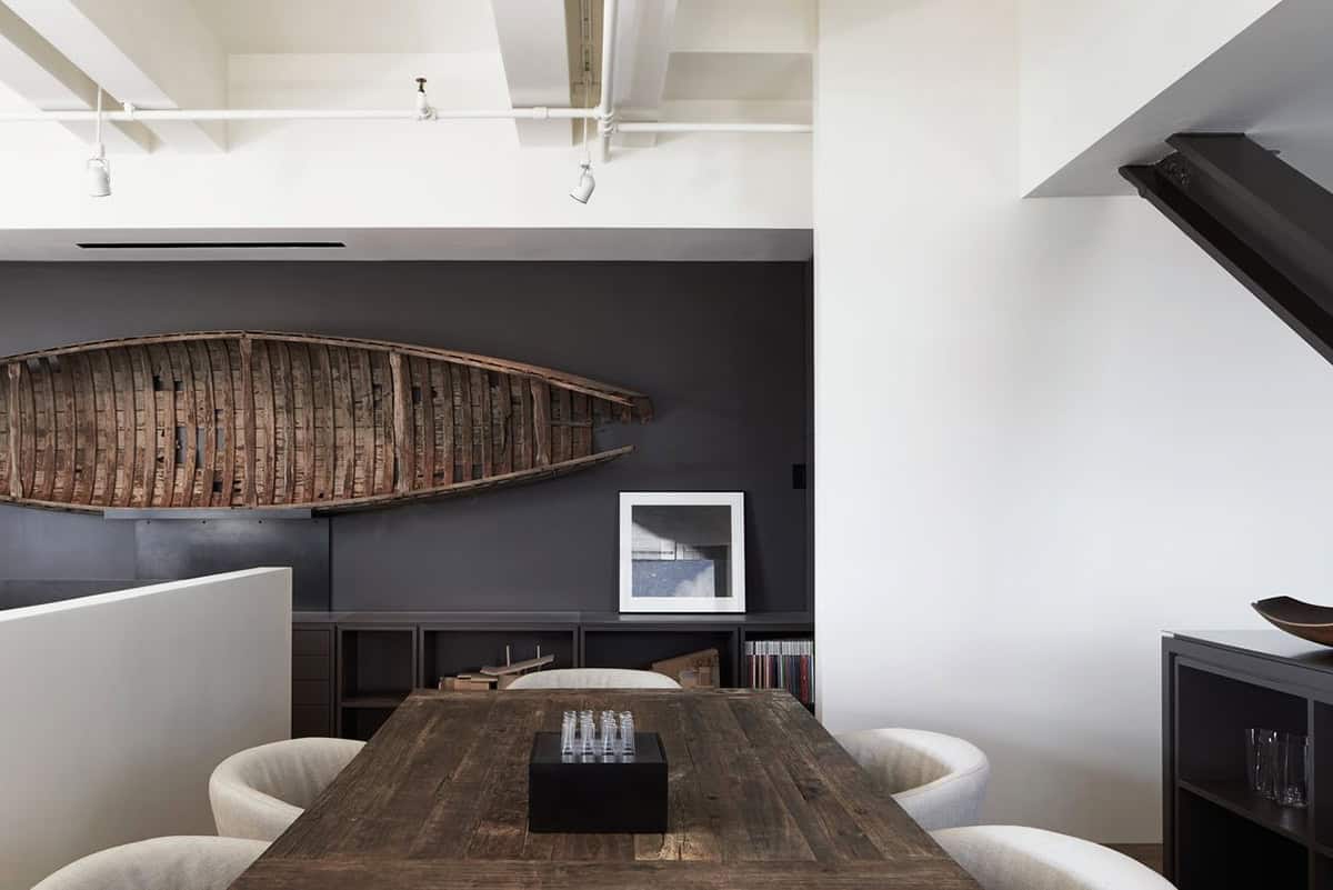 Dining area with a reclaimed wood table, curved cream upholstered chairs, and an antique wooden canoe displayed on a dark accent wall above low shelving