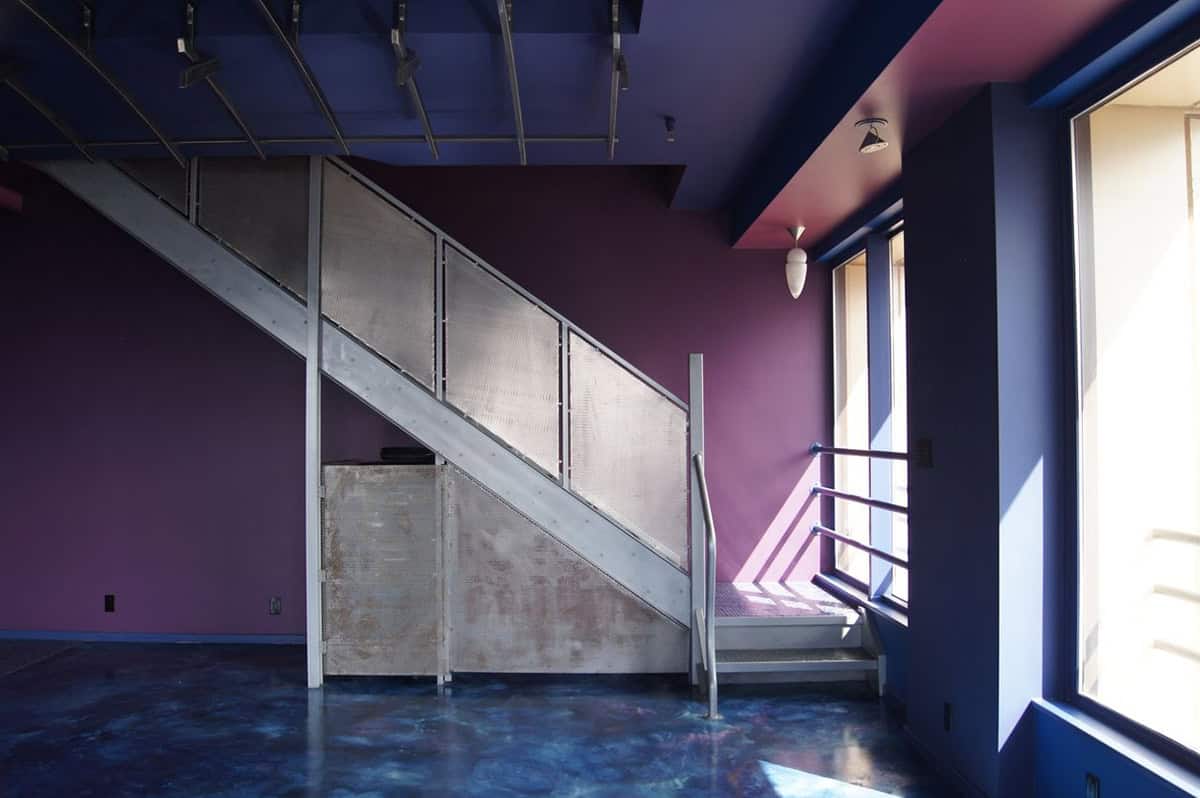 Lower level with bold purple and blue painted walls, polished concrete floors, industrial steel mesh staircase, and track lighting on the ceiling