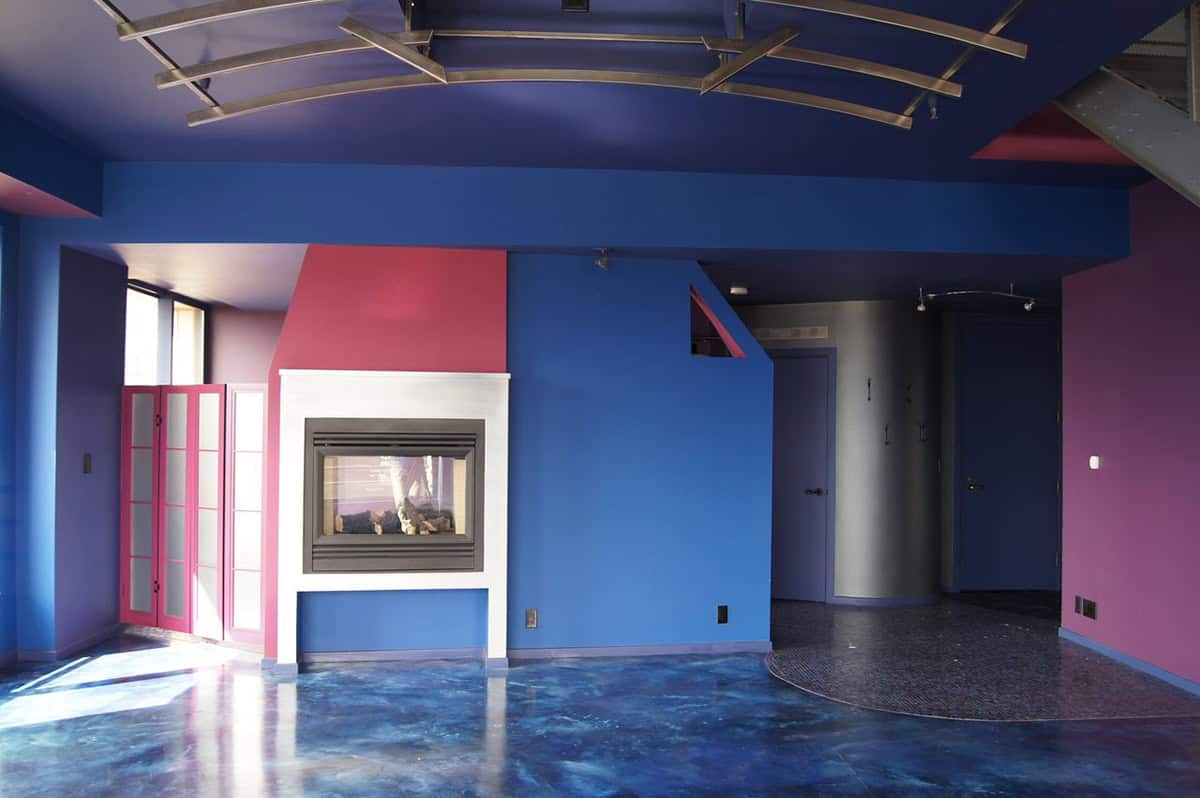 Living space with electric blue, crimson, and purple walls, epoxy-finished concrete floors, a two-sided fireplace, and curved track lighting above