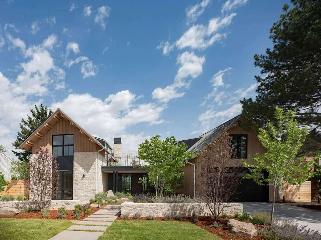 Modern farmhouse exterior with stone base, vertical wood siding, and steep gabled roof, surrounded by landscaped garden