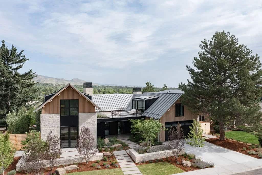 Aerial view of contemporary home with standing-seam metal roof, stone chimneys, and mountain views in the background