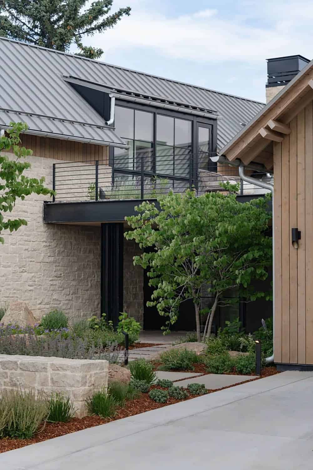 Close-up of stone and wood exterior with black-framed balcony and second-story windows above entry