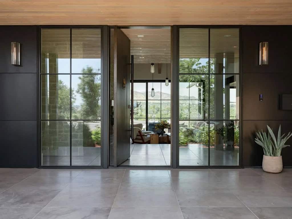 Glass-walled entryway with black steel-framed doors opening to a view of mountains and outdoor seating