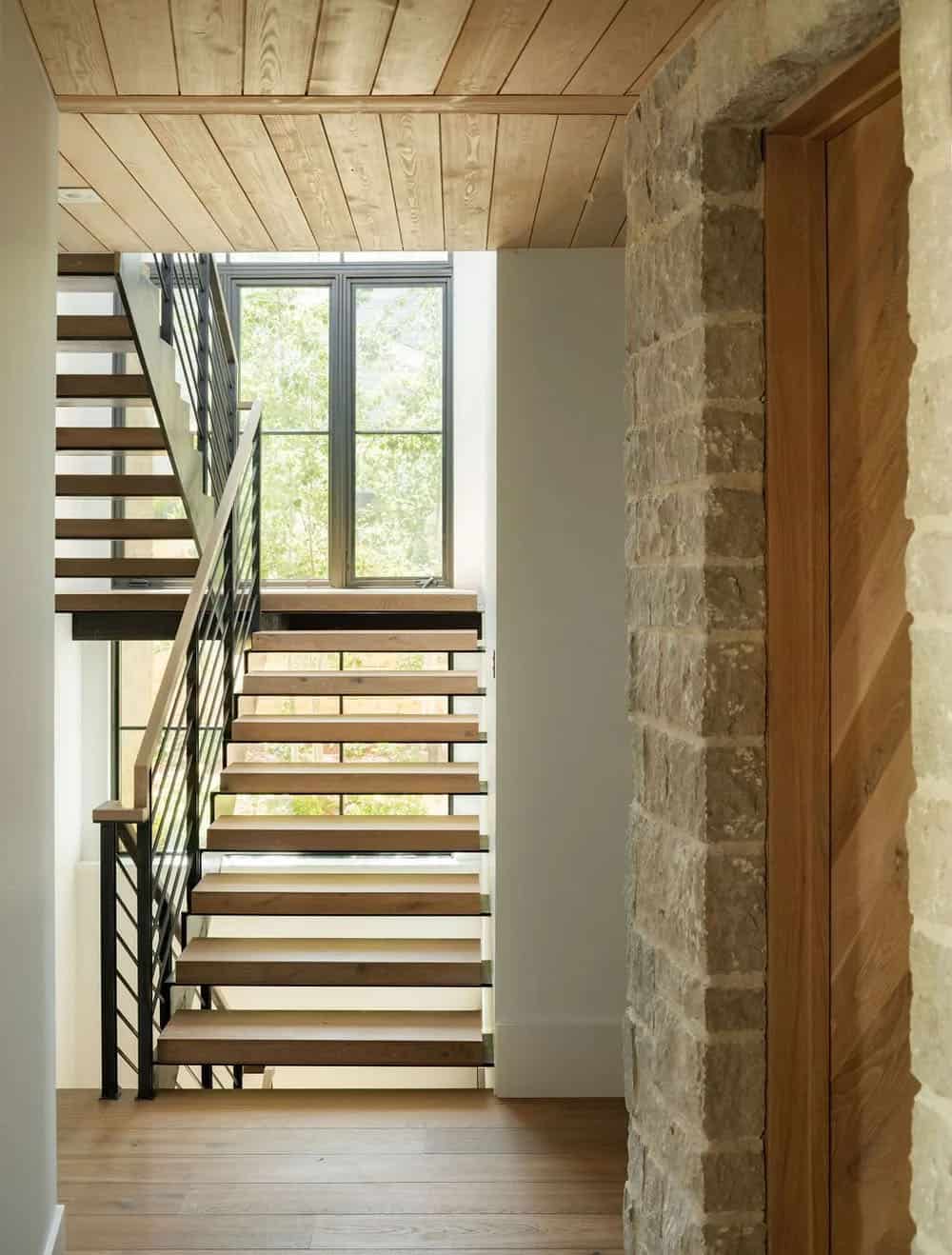 Floating wood and steel staircase beside a stone archway leading to the wood front door