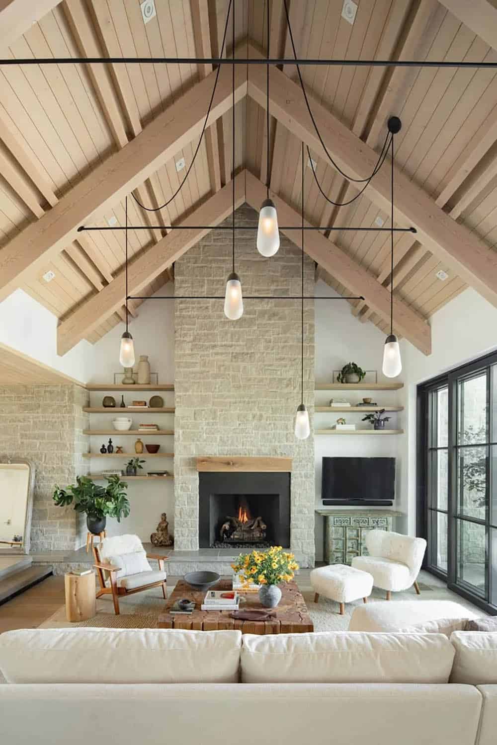 Living room with peaked wood-beamed ceiling, stone fireplace wall, and hanging glass pendant lights