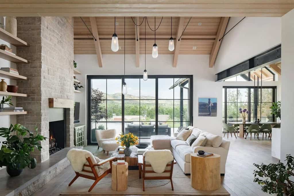 Open-concept living and dining area with stone fireplace, sheepskin-draped chairs, and mountain-view windows
