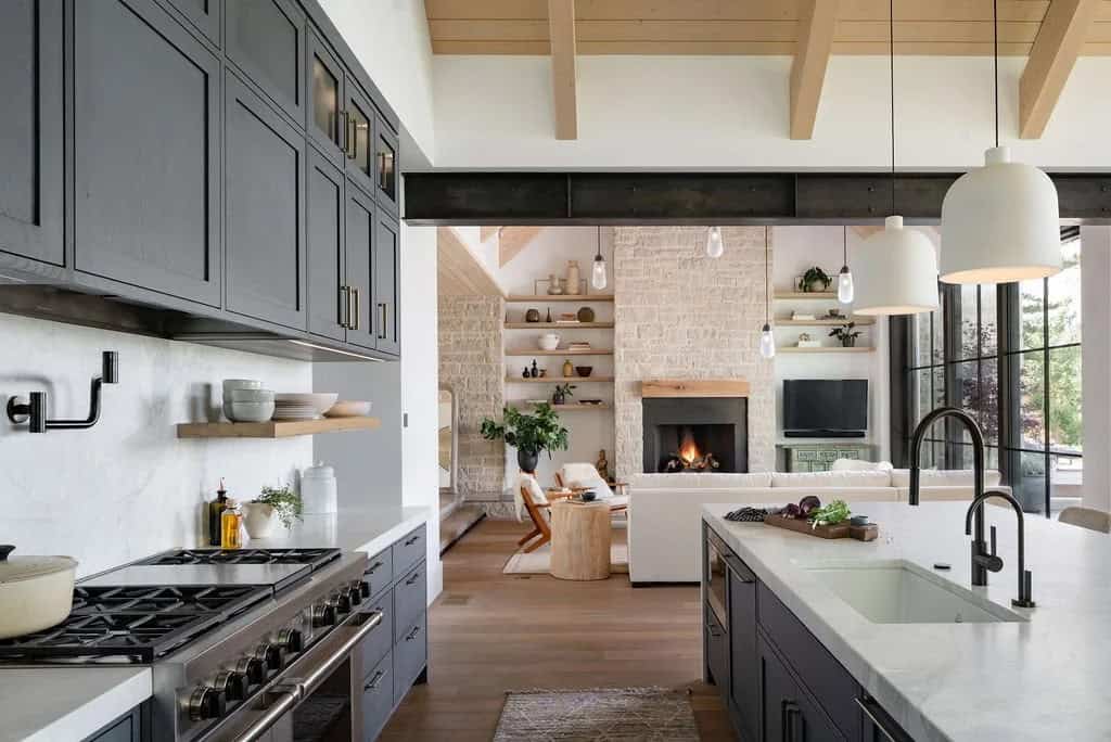 Kitchen with charcoal cabinetry and white countertops opening to a living room with stone fireplace