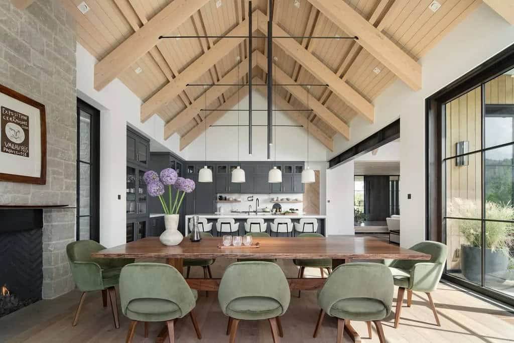 Dining room with live-edge wood table, green velvet chairs, and soaring wood-beamed cathedral ceiling