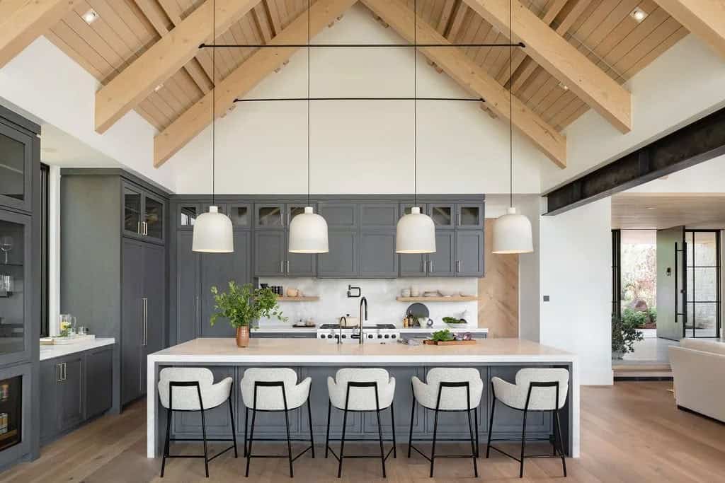 Kitchen island with white oak stools and gray cabinetry beneath a vaulted wood-beamed ceiling