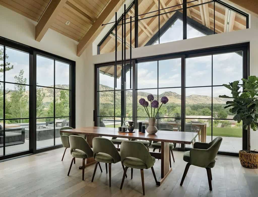 Floor-to-ceiling black-framed windows in dining room showcasing mountain views beyond a wood dining table