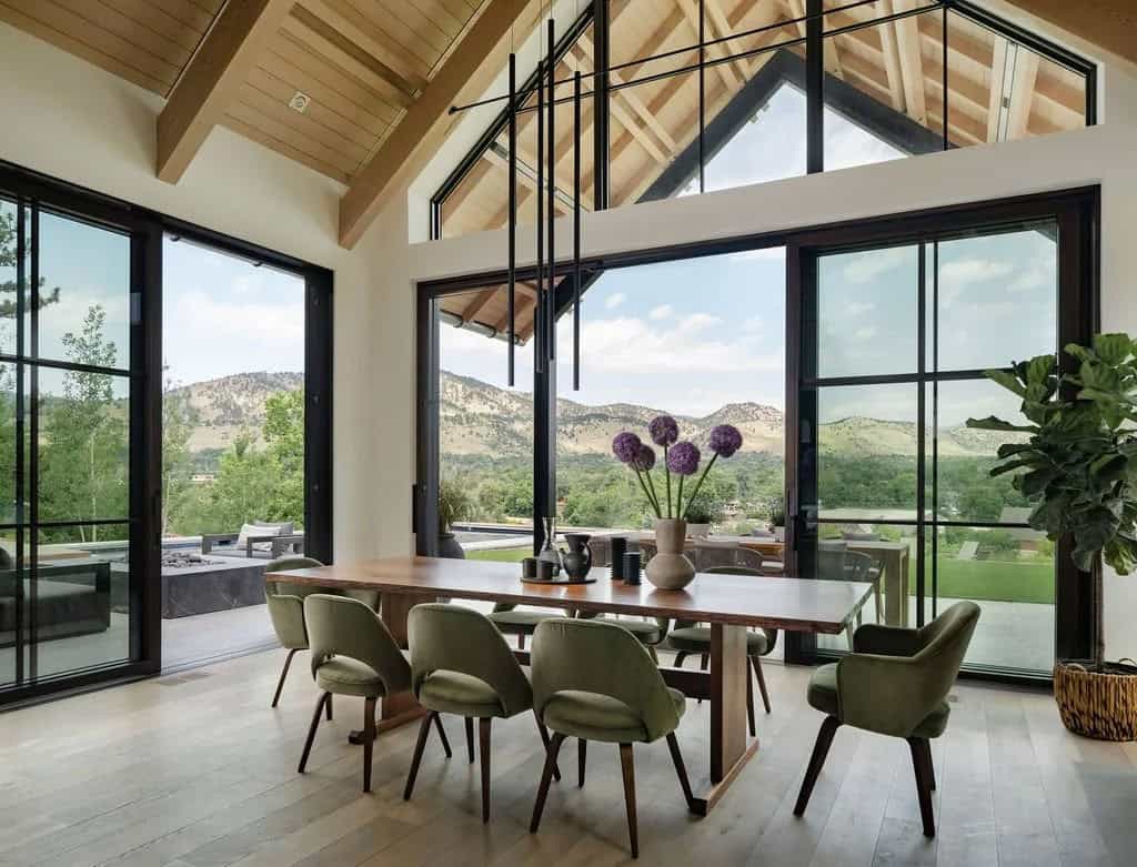 Dining area with green chairs and expansive glass walls framing rolling foothill scenery