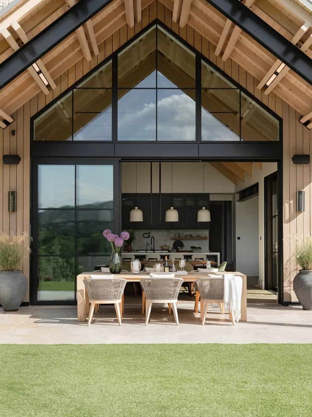 Covered outdoor dining patio under a glass gable peak, overlooking a green lawn with mountain views