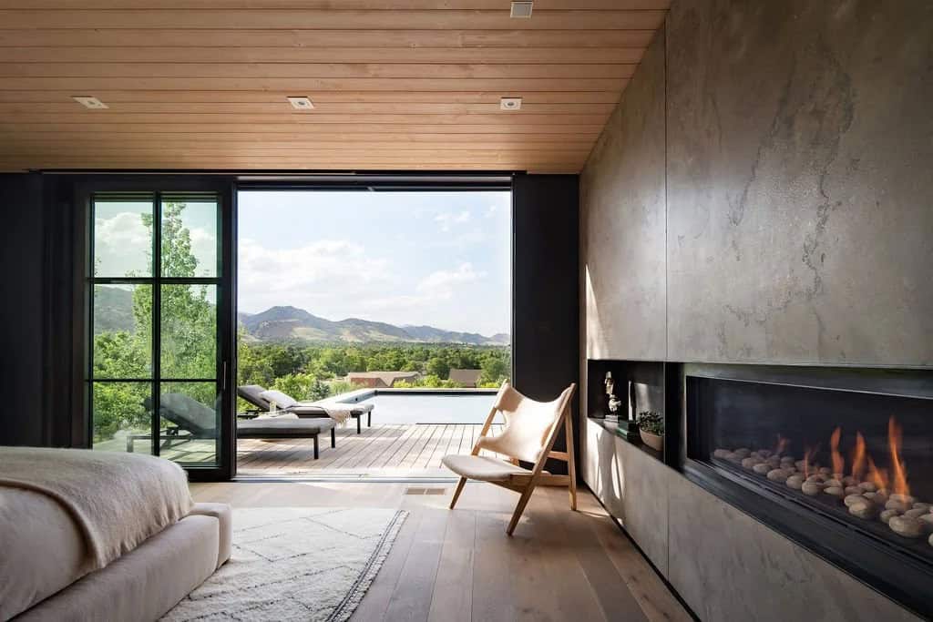 Primary bedroom with sliding glass wall opening to pool deck and mountain view, stone fireplace, and wood-clad ceiling