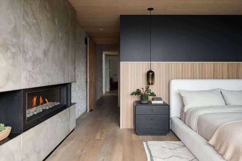 Bedroom with stone fireplace, dark accent wall, slatted wood panel headboard, and hallway view