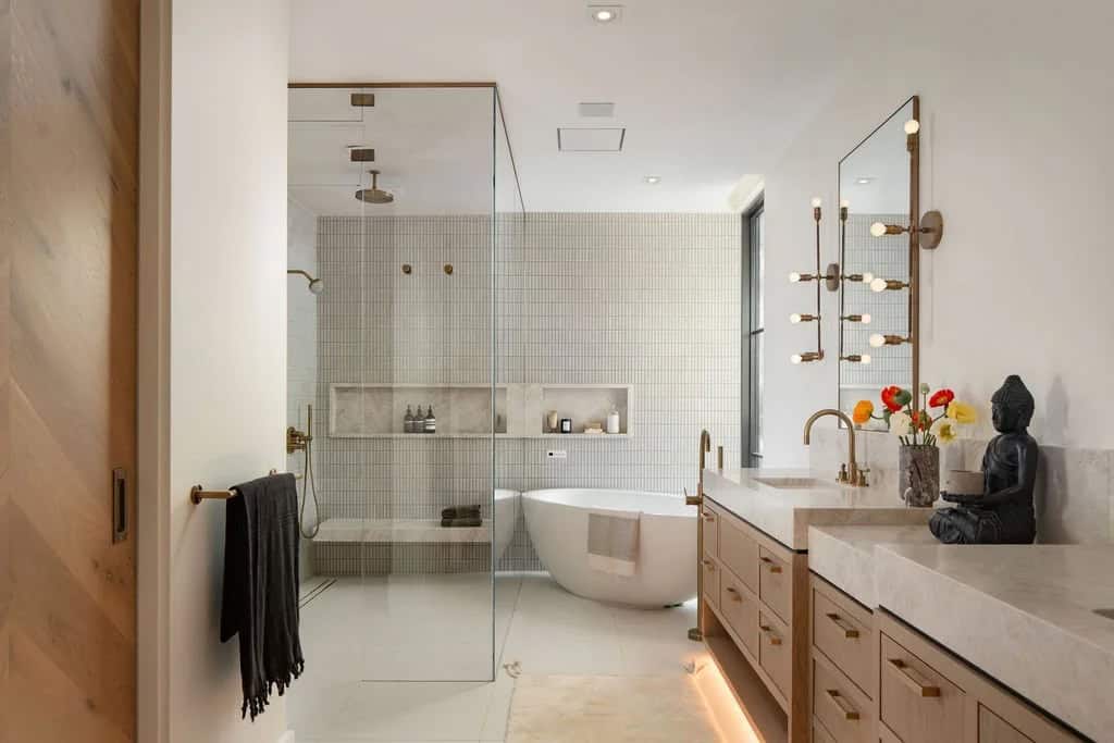 Spa-style bathroom with freestanding soaking tub, glass shower, wood vanity, and brass fixtures