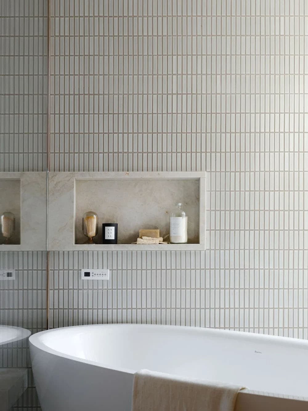 Detail of vertical tile wall with built-in marble niche shelf above a freestanding white bathtub