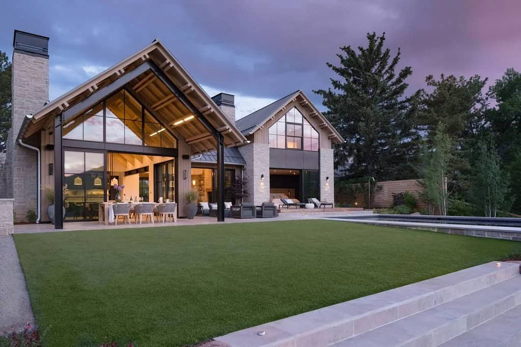 Twilight view of the home's expansive rear lawn, glass gables, and stone terrace steps