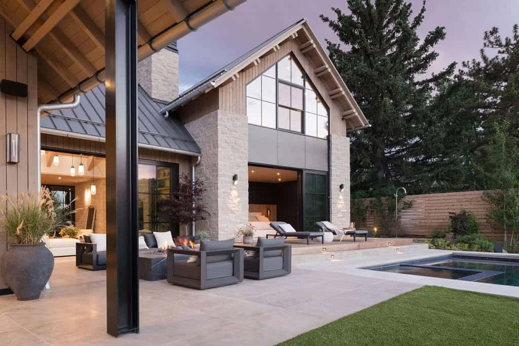 Twilight patio with fire feature, gray lounge chairs, pool, and glass gable facade of the home