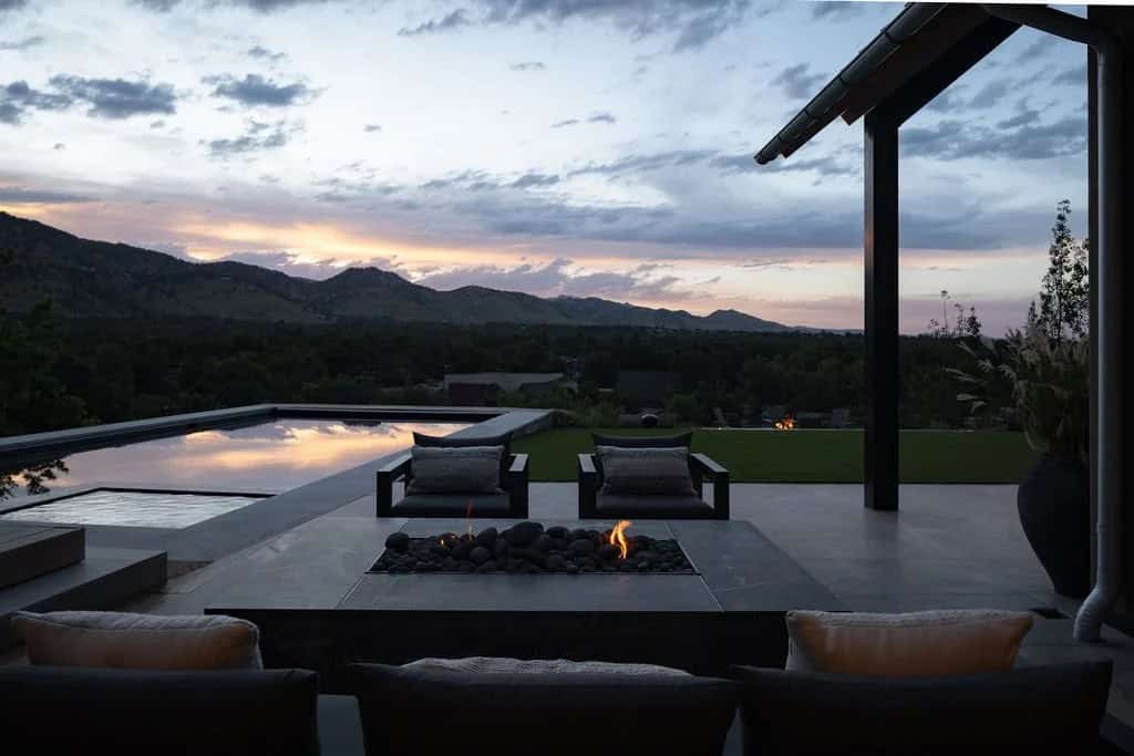 Fire pit lounge area at dusk beside an infinity-edge pool with mountain silhouette in the distance