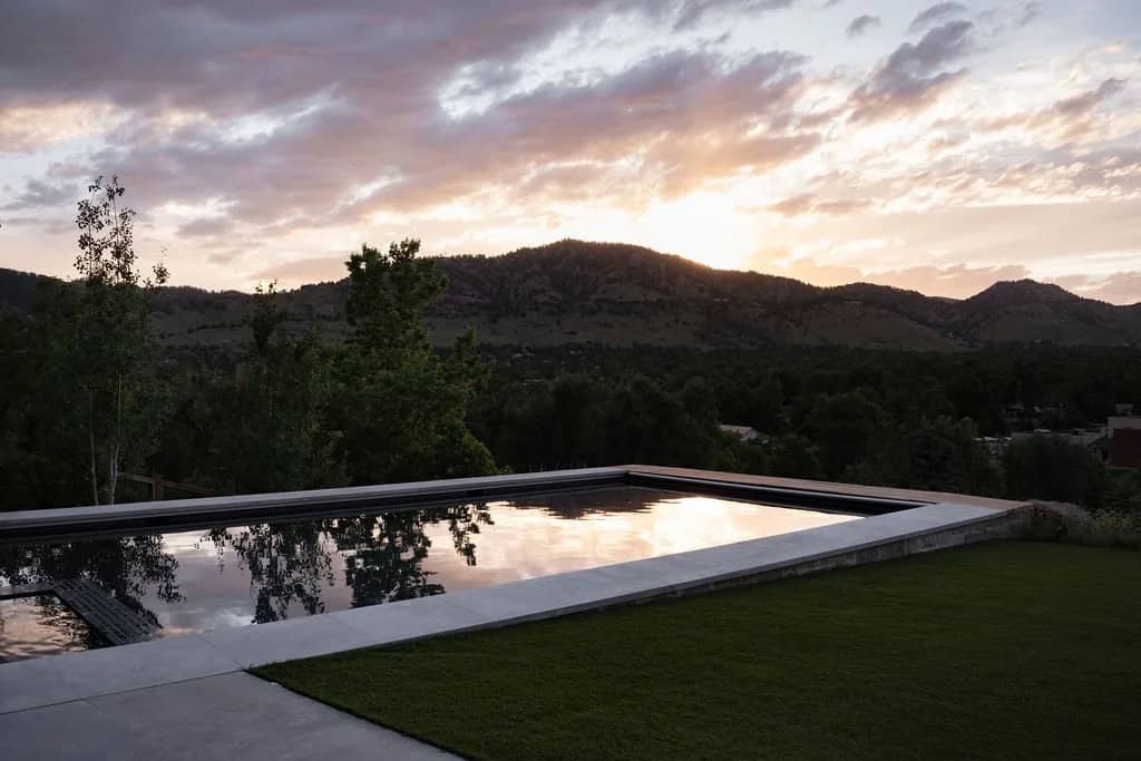 Sunset reflecting on a rectangular pool's still water with mountain backdrop and lawn foreground