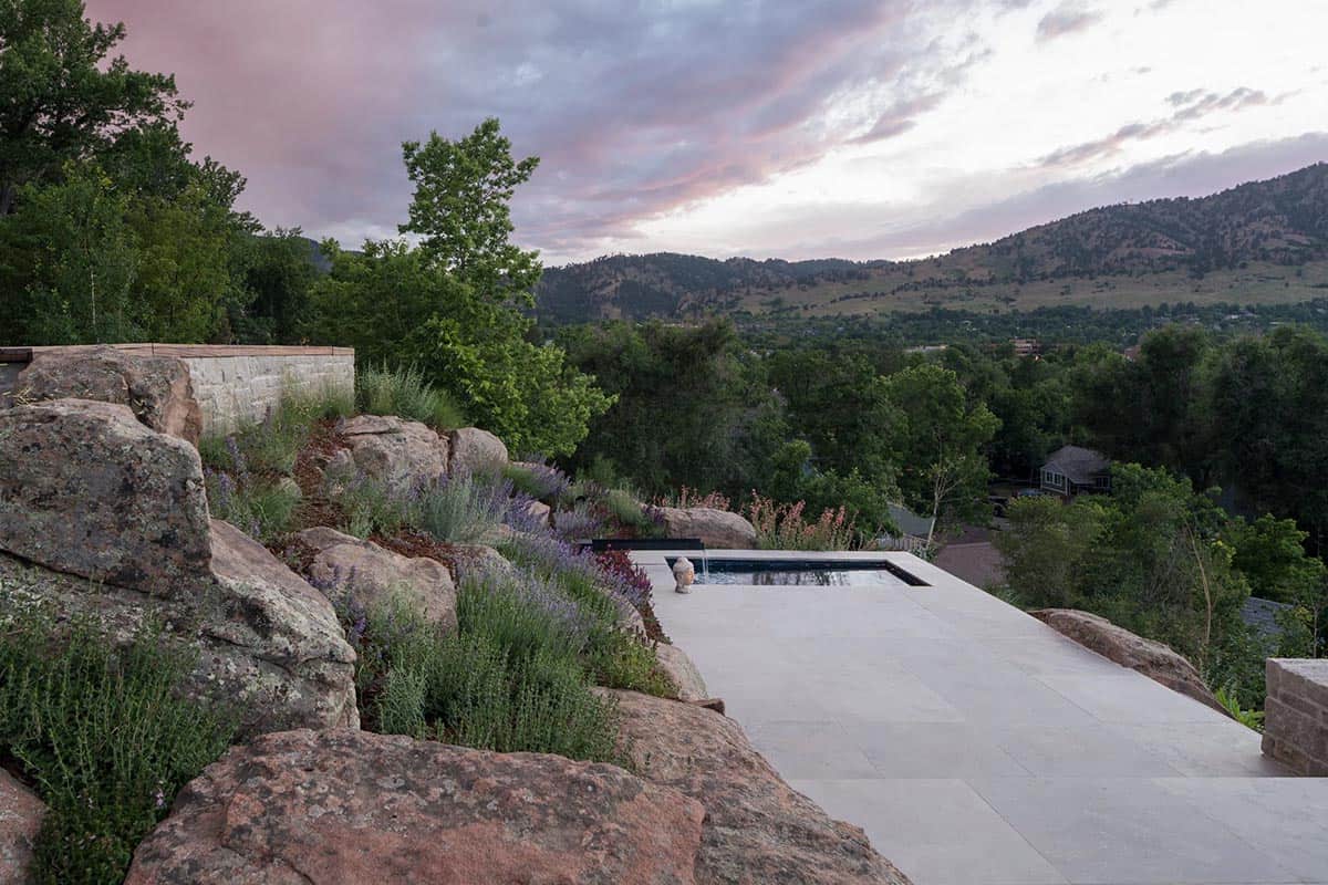 Stone patio with small reflecting pool perched above a boulder-terraced hillside at dusk